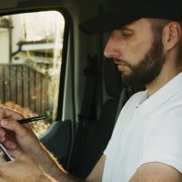 A delivery driver sits in a van, writing on a clipboard, capturing essential details. Daytime.